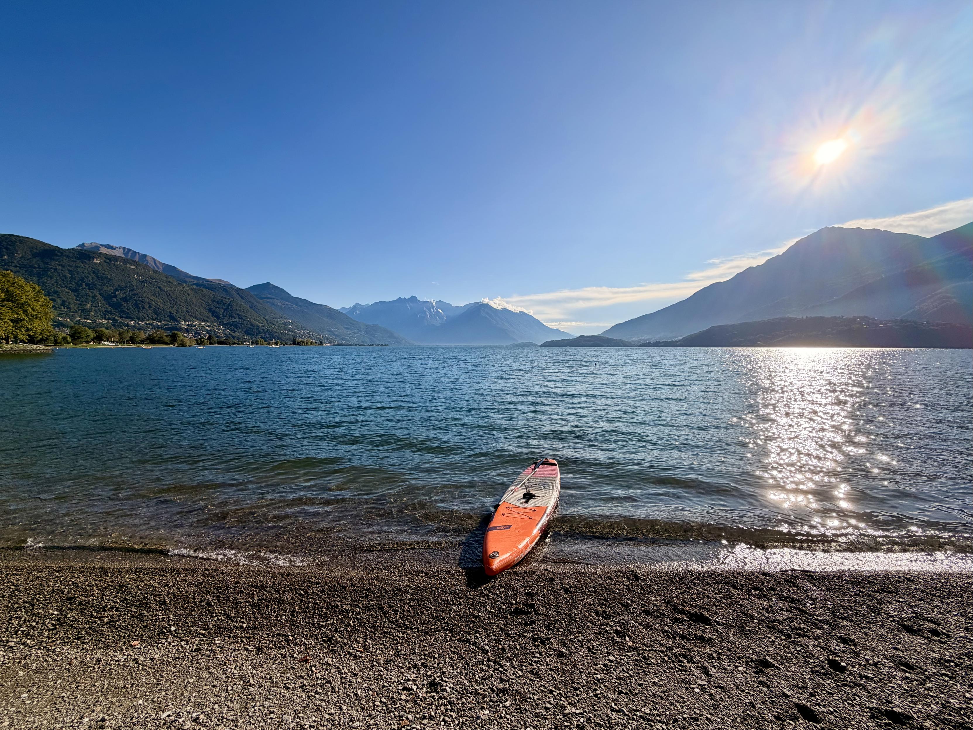 SUP-Board am Strand des Comer See im Sonnenlicht mit blauem wolkenlosen Himmel.