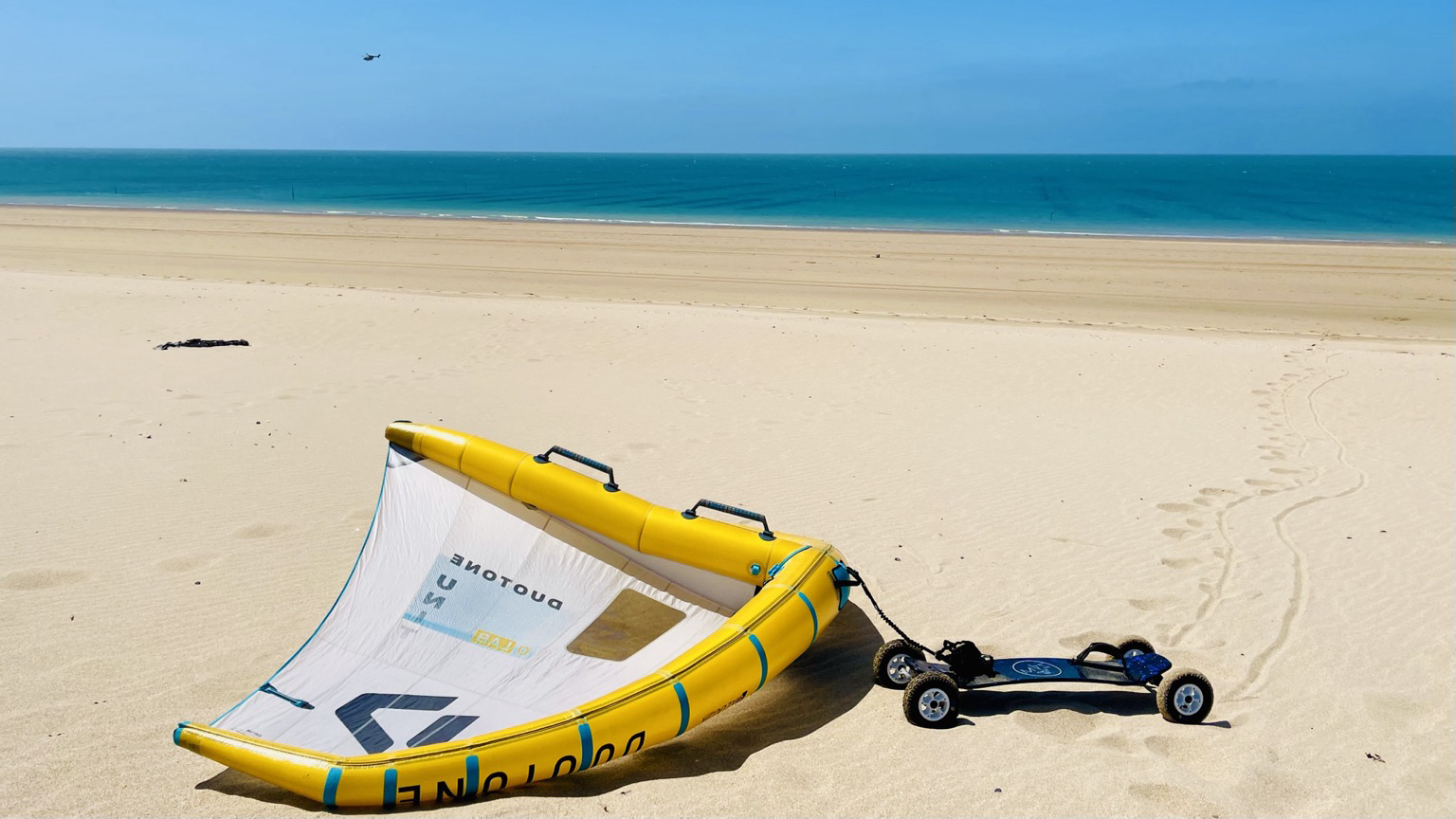 Ein Strand in der Bretagne. Zu sehen mit dem Meer im Hintergrund ist auf dem Strand ein Moutainboard und ein Duotone-Wing zu sehen. 